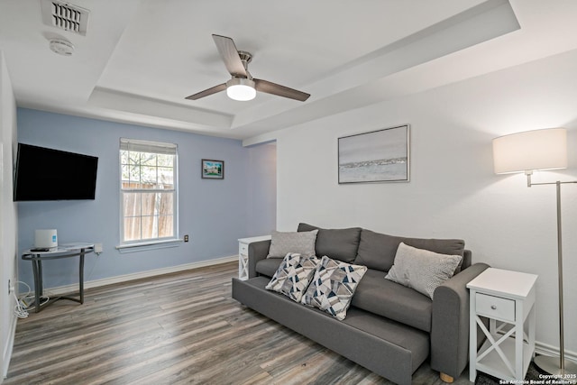 living room with dark wood-type flooring, ceiling fan, and a tray ceiling