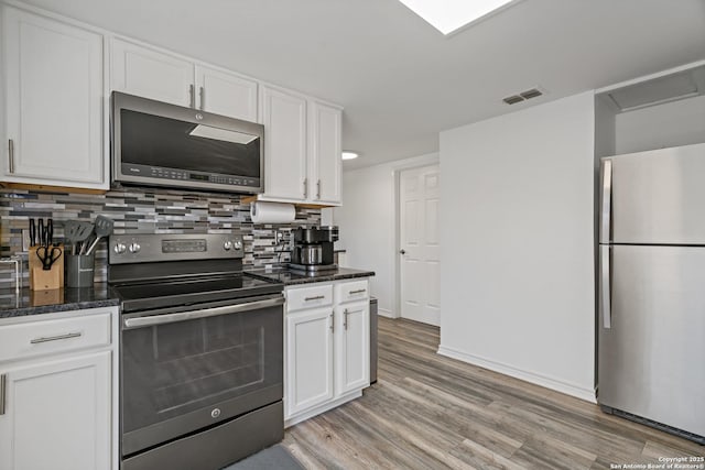 kitchen featuring white cabinetry, appliances with stainless steel finishes, decorative backsplash, and dark stone counters