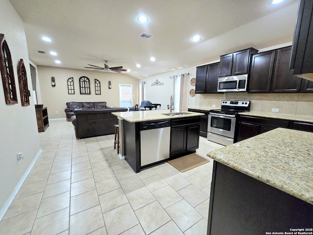 kitchen with appliances with stainless steel finishes, sink, backsplash, ceiling fan, and a center island with sink