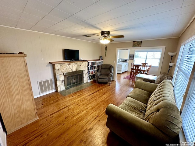 living room with ornamental molding, a stone fireplace, hardwood / wood-style floors, and ceiling fan