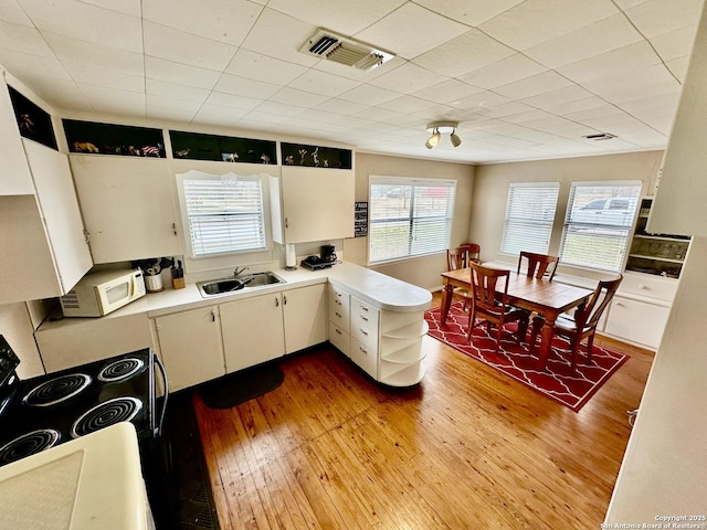 kitchen featuring sink, light wood-type flooring, kitchen peninsula, black range with electric stovetop, and white cabinets