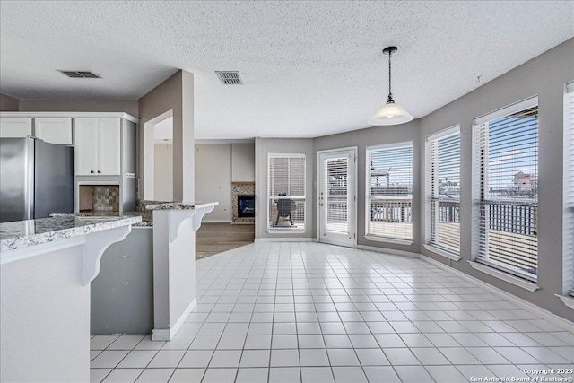 kitchen with pendant lighting, white cabinets, stainless steel fridge, a kitchen bar, and light tile patterned floors