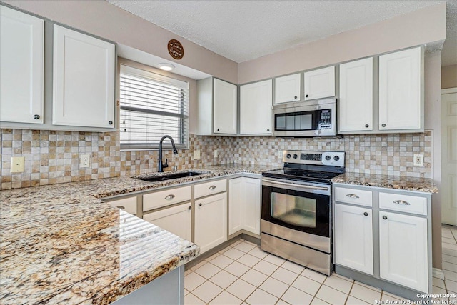 kitchen featuring sink, appliances with stainless steel finishes, white cabinetry, light stone counters, and tasteful backsplash