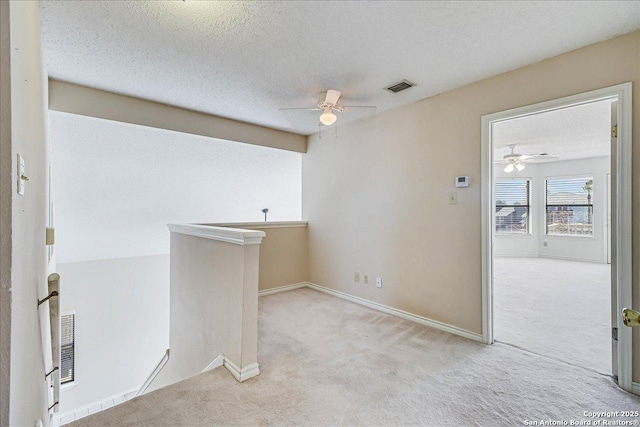 unfurnished room featuring ceiling fan, light carpet, and a textured ceiling