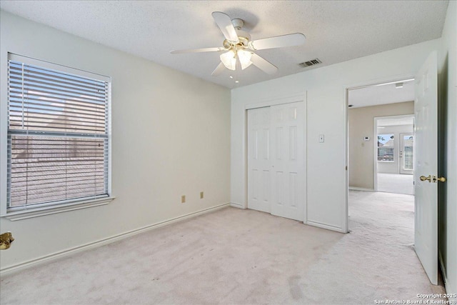 unfurnished bedroom featuring light carpet, a textured ceiling, and ceiling fan