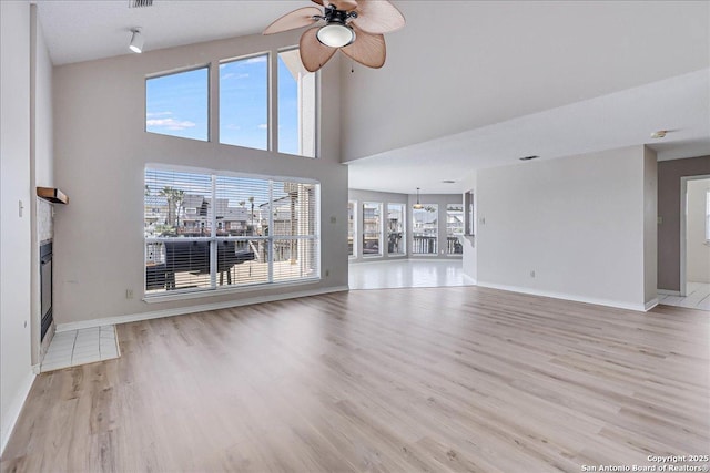 unfurnished living room featuring a towering ceiling, light hardwood / wood-style flooring, ceiling fan, and plenty of natural light