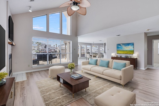 living room with ceiling fan, light hardwood / wood-style floors, and a towering ceiling