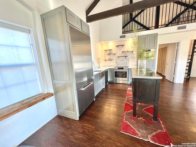 kitchen with a kitchen island, appliances with stainless steel finishes, high vaulted ceiling, beamed ceiling, and dark hardwood / wood-style flooring