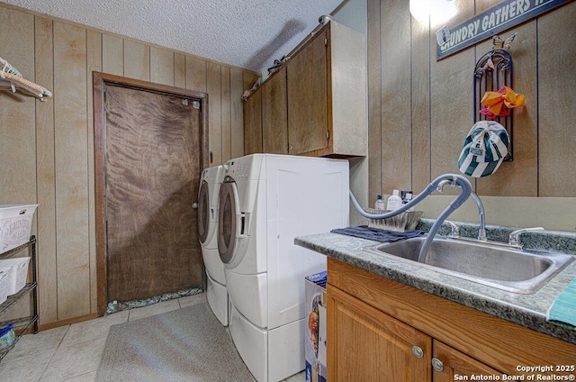 clothes washing area with washing machine and clothes dryer, sink, cabinets, a textured ceiling, and wooden walls