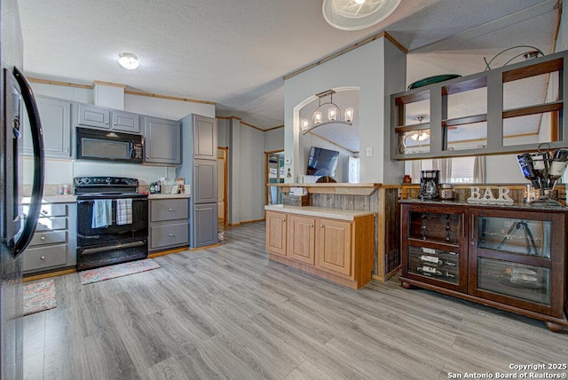 kitchen featuring crown molding, gray cabinetry, black appliances, light hardwood / wood-style floors, and vaulted ceiling