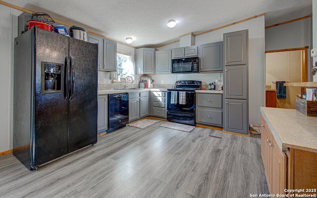 kitchen featuring sink, black appliances, a textured ceiling, and light wood-type flooring