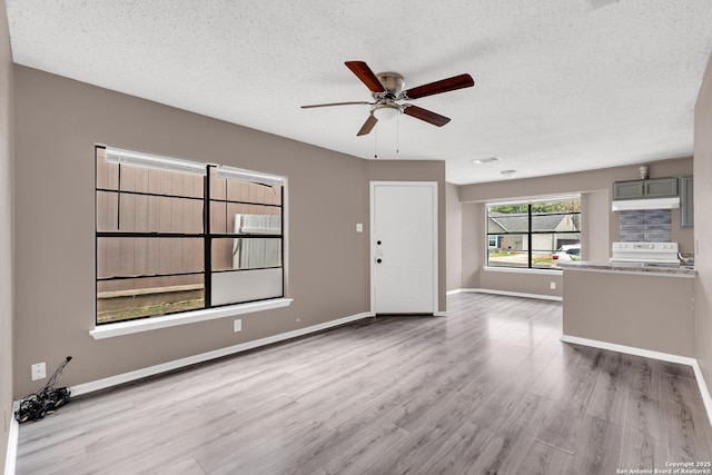 unfurnished living room featuring ceiling fan, light hardwood / wood-style floors, and a textured ceiling