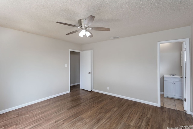 unfurnished bedroom with ceiling fan, ensuite bathroom, dark hardwood / wood-style flooring, and a textured ceiling