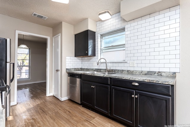 kitchen featuring appliances with stainless steel finishes, sink, light wood-type flooring, decorative backsplash, and a textured ceiling