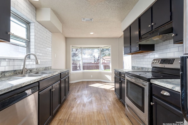 kitchen with sink, a textured ceiling, stainless steel appliances, decorative backsplash, and exhaust hood