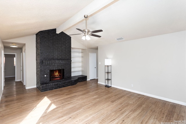 unfurnished living room with hardwood / wood-style floors, a fireplace, lofted ceiling with beams, ceiling fan, and a textured ceiling