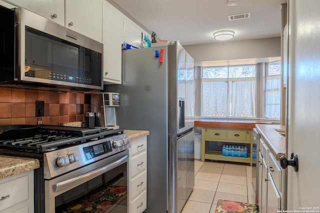 kitchen with light tile patterned floors, visible vents, white cabinets, appliances with stainless steel finishes, and backsplash