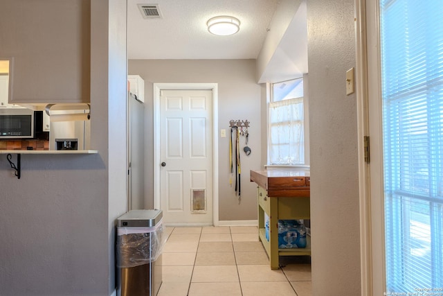 interior space featuring light tile patterned floors, a textured ceiling, visible vents, and baseboards