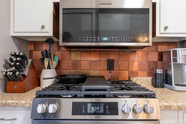 kitchen with white cabinetry, appliances with stainless steel finishes, light stone countertops, and backsplash