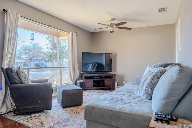 living area with a wealth of natural light, visible vents, a textured ceiling, and wood finished floors