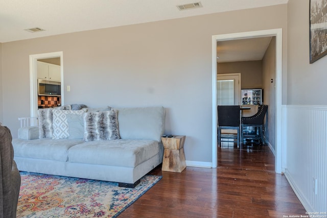 living room with a wainscoted wall, baseboards, visible vents, and wood finished floors