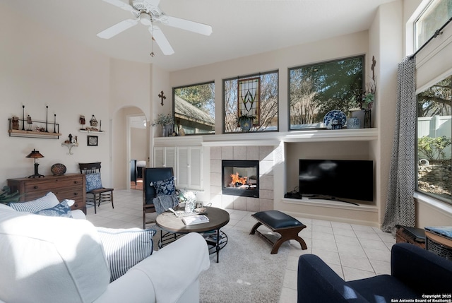 living room featuring ceiling fan, a tiled fireplace, and light tile patterned floors