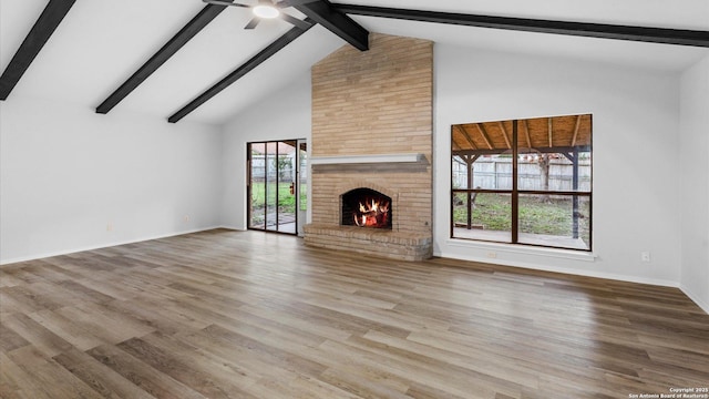 unfurnished living room with high vaulted ceiling, beamed ceiling, wood-type flooring, ceiling fan, and a brick fireplace