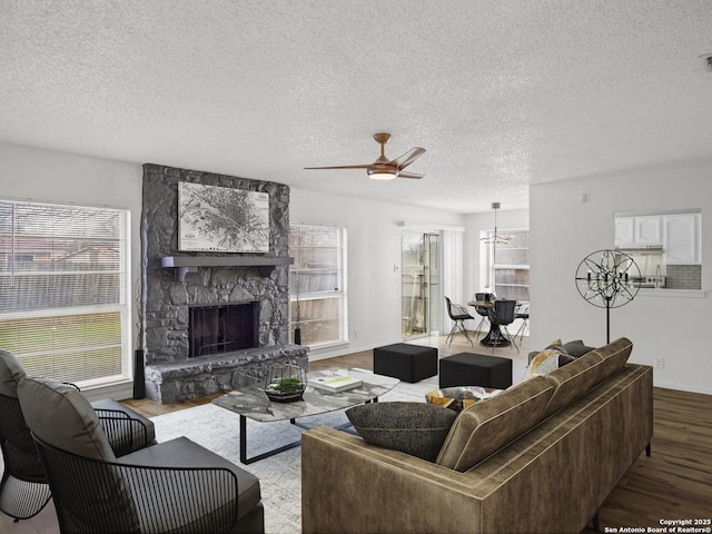 living room with ceiling fan with notable chandelier, a fireplace, light hardwood / wood-style floors, and a textured ceiling