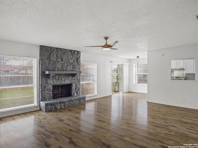 unfurnished living room with dark hardwood / wood-style flooring, a fireplace, ceiling fan with notable chandelier, and plenty of natural light