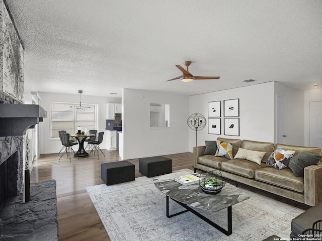 living room featuring ceiling fan, wood-type flooring, a stone fireplace, and a textured ceiling