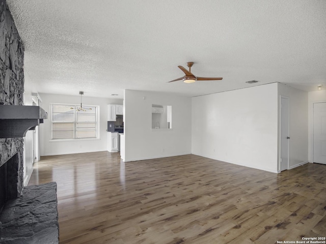 unfurnished living room featuring a stone fireplace, a textured ceiling, dark hardwood / wood-style floors, and ceiling fan