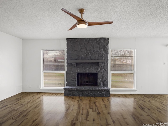 unfurnished living room with wood-type flooring, a stone fireplace, ceiling fan, and a textured ceiling