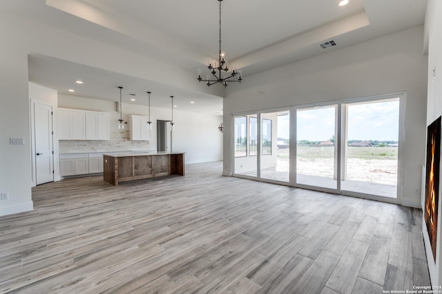 kitchen featuring a spacious island, white cabinetry, decorative light fixtures, light wood-type flooring, and a raised ceiling