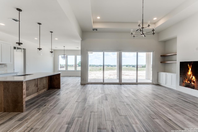 unfurnished living room with an inviting chandelier, built in features, and light hardwood / wood-style flooring