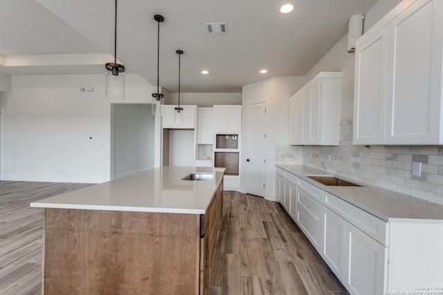 kitchen with a large island, hanging light fixtures, white cabinets, and light wood-type flooring