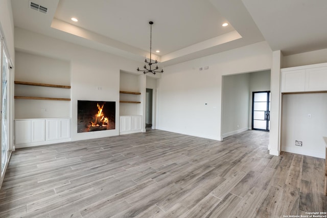 unfurnished living room featuring built in shelves, a tray ceiling, and light hardwood / wood-style floors