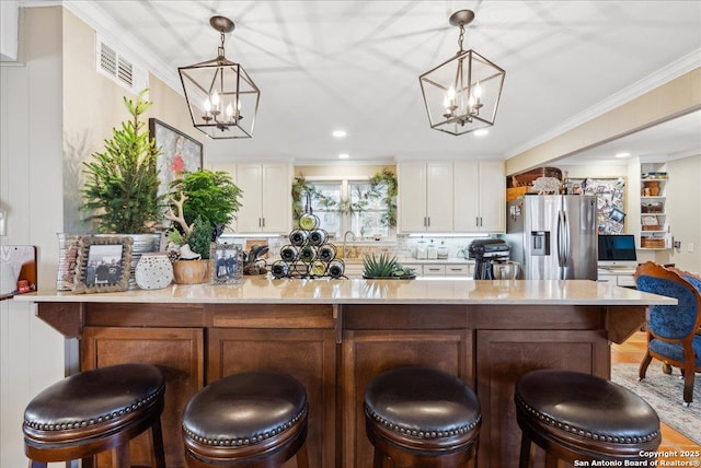 kitchen with stainless steel refrigerator with ice dispenser, crown molding, a chandelier, hanging light fixtures, and white cabinets