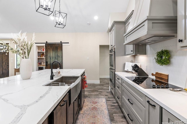 kitchen with premium range hood, pendant lighting, stainless steel appliances, a barn door, and dark wood-type flooring