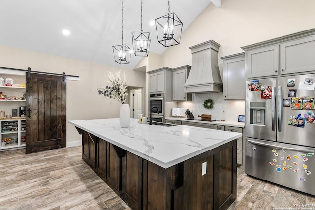 kitchen with premium range hood, appliances with stainless steel finishes, light stone counters, decorative backsplash, and a barn door