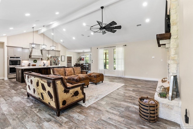 living room with ceiling fan, a stone fireplace, and vaulted ceiling with beams