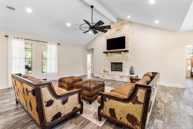 living room with ceiling fan, beam ceiling, light hardwood / wood-style floors, and a stone fireplace