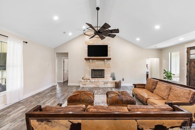 living room with a stone fireplace, vaulted ceiling, a wealth of natural light, ceiling fan, and light hardwood / wood-style floors