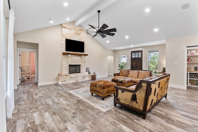 living room with vaulted ceiling with beams, ceiling fan, a stone fireplace, and light wood-type flooring