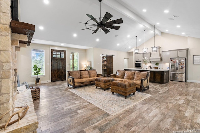 living room with beam ceiling, high vaulted ceiling, light hardwood / wood-style flooring, ceiling fan, and a barn door