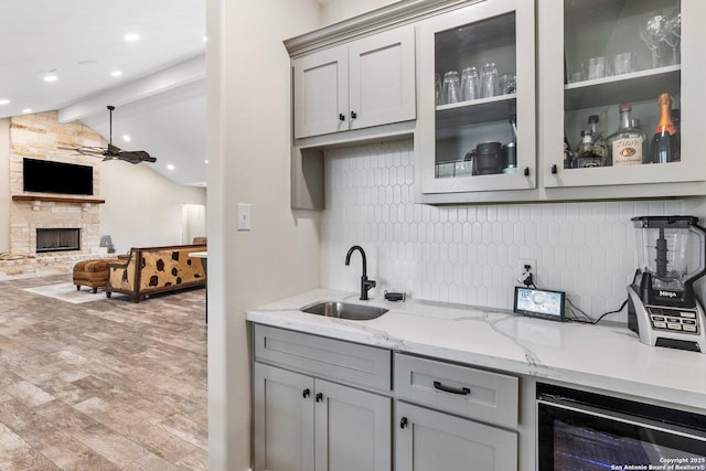 bar featuring gray cabinets, a stone fireplace, sink, and wine cooler