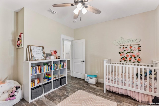 bedroom with dark hardwood / wood-style flooring, a nursery area, and ceiling fan