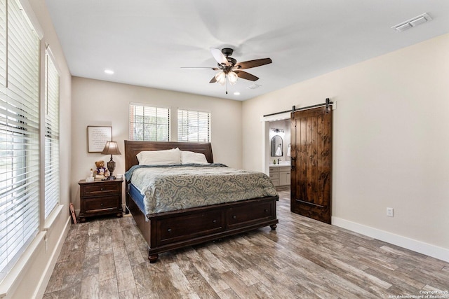 bedroom featuring hardwood / wood-style floors, sink, ceiling fan, a barn door, and ensuite bath