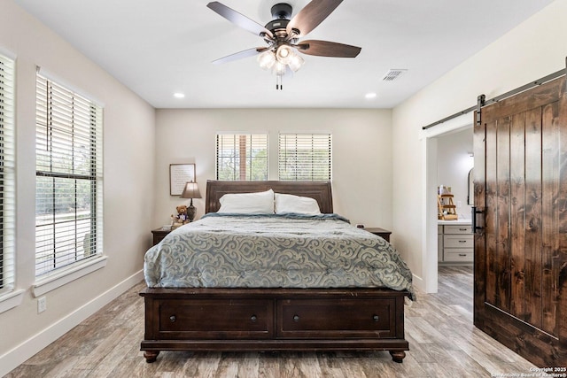 bedroom featuring a barn door, light wood-type flooring, ceiling fan, and ensuite bath