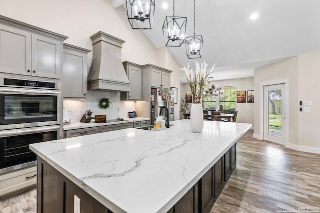 kitchen with lofted ceiling, sink, appliances with stainless steel finishes, an island with sink, and custom range hood