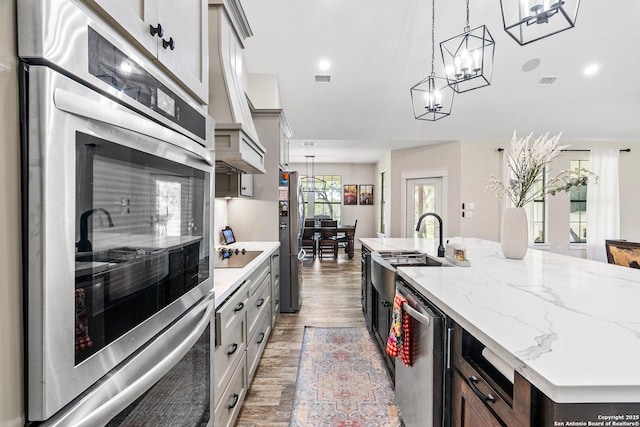 kitchen with pendant lighting, sink, dark wood-type flooring, appliances with stainless steel finishes, and a center island with sink